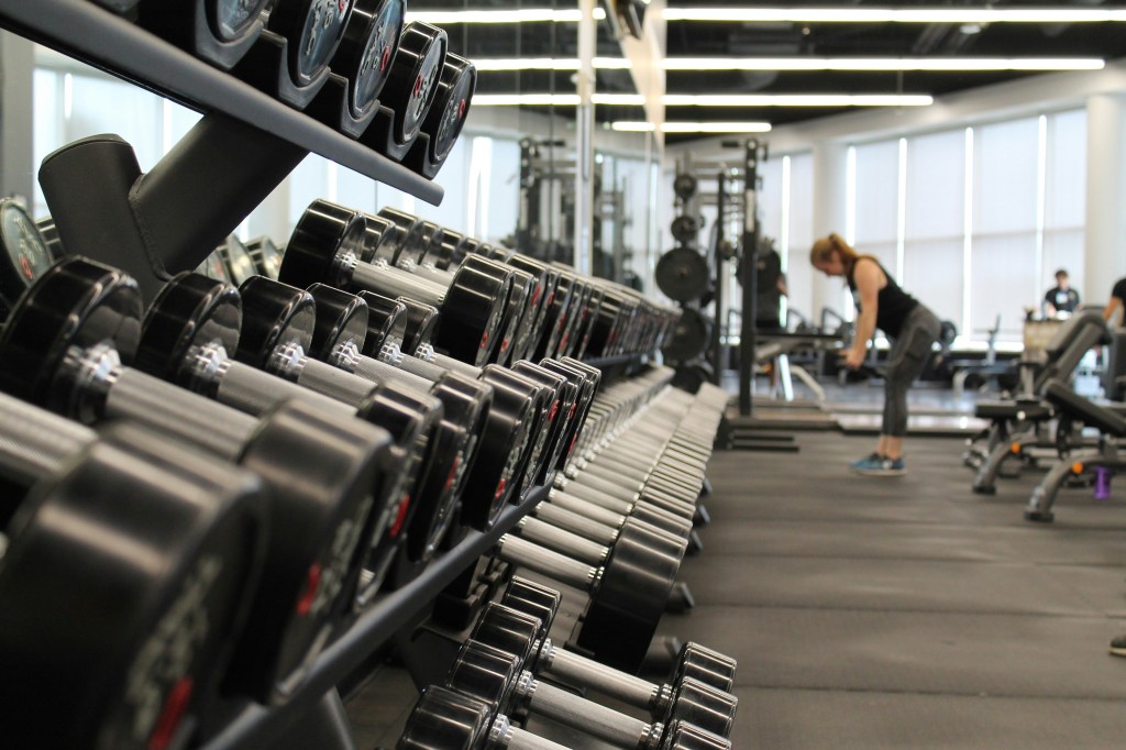 Dumbbells sit side by side in a workout studio with a woman in the background lifting weights.